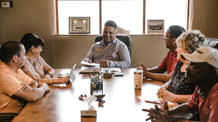 A diverse team of nonprofit professionals discussing projects around an office table 